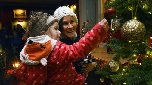 Woman holding little girl, looking at the baubles on the Christmas tree at Saltram in Devon.